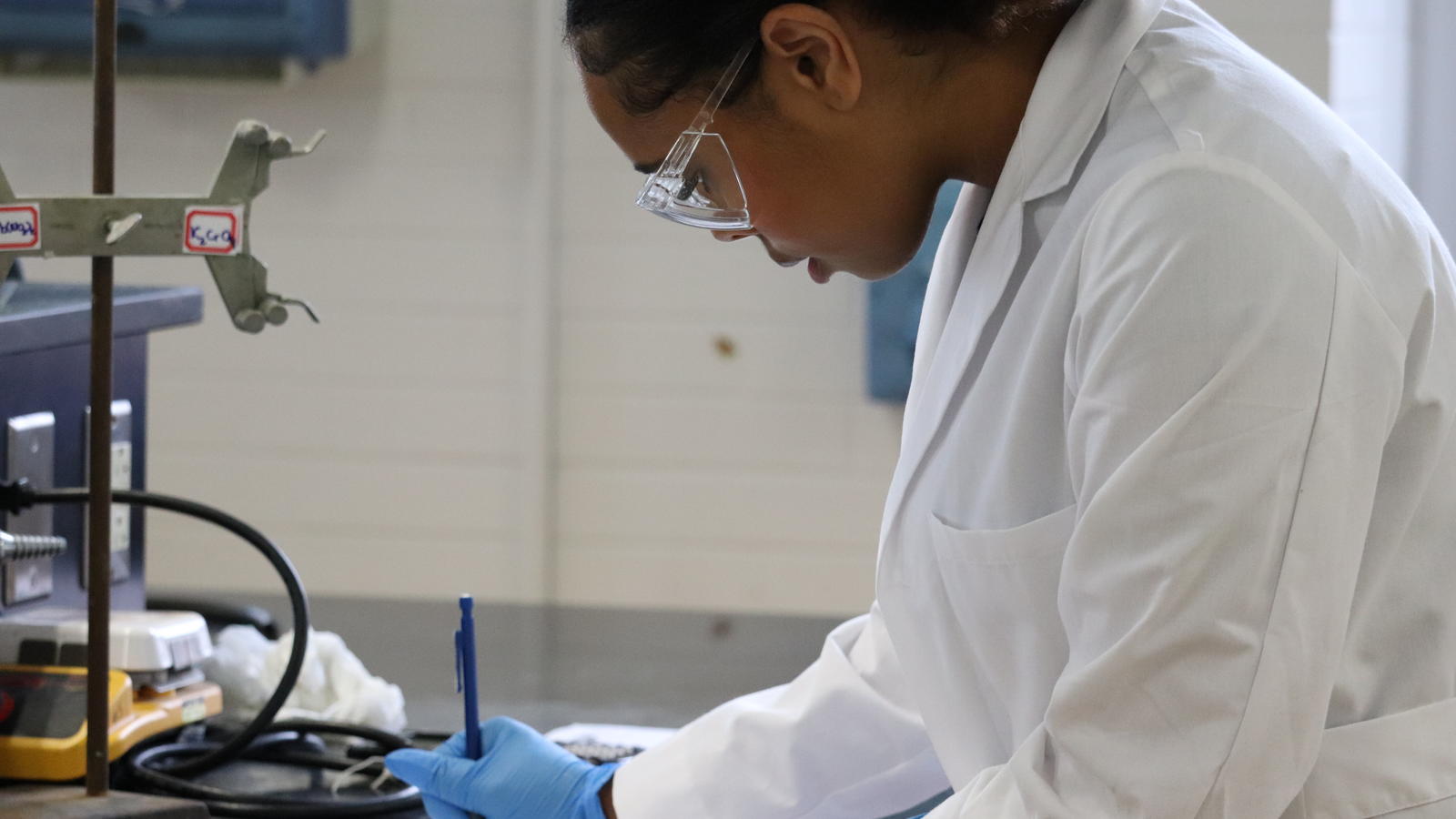 Student Writing in Lab Coat and Safety Glasses